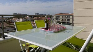 A balcony with a glass table and chairs, a bottle of wine, and a tray of glasses.