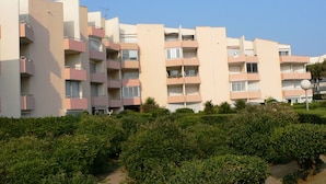 Un edificio residencial de varios pisos con balcones, cielo despejado y abundante vegetación en primer plano.