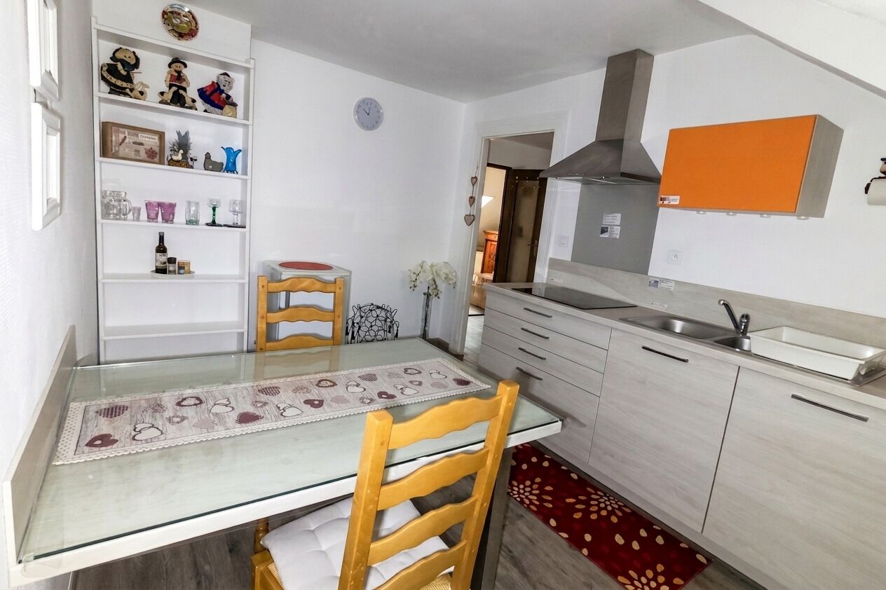 Una cocina compacta con mesa, sillas, horno empotrado y un refrigerador pequeño.