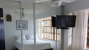 A bedroom with a bed, a TV, a ceiling fan, and a window with bars. - El Encanto de Naturaleza y Romantic! Apartment 2 (Fajardo)