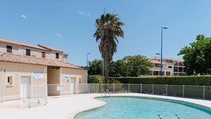 Une piscine à bordures courbes, entourée d’une clôture blanche, avec un palmier à proximité.