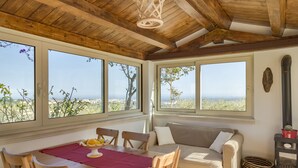 A cozy room with a wooden ceiling, large windows, a sofa, a table with a placemat, and a wood-burning stove. - Tenuta Olive Alive (Noto)