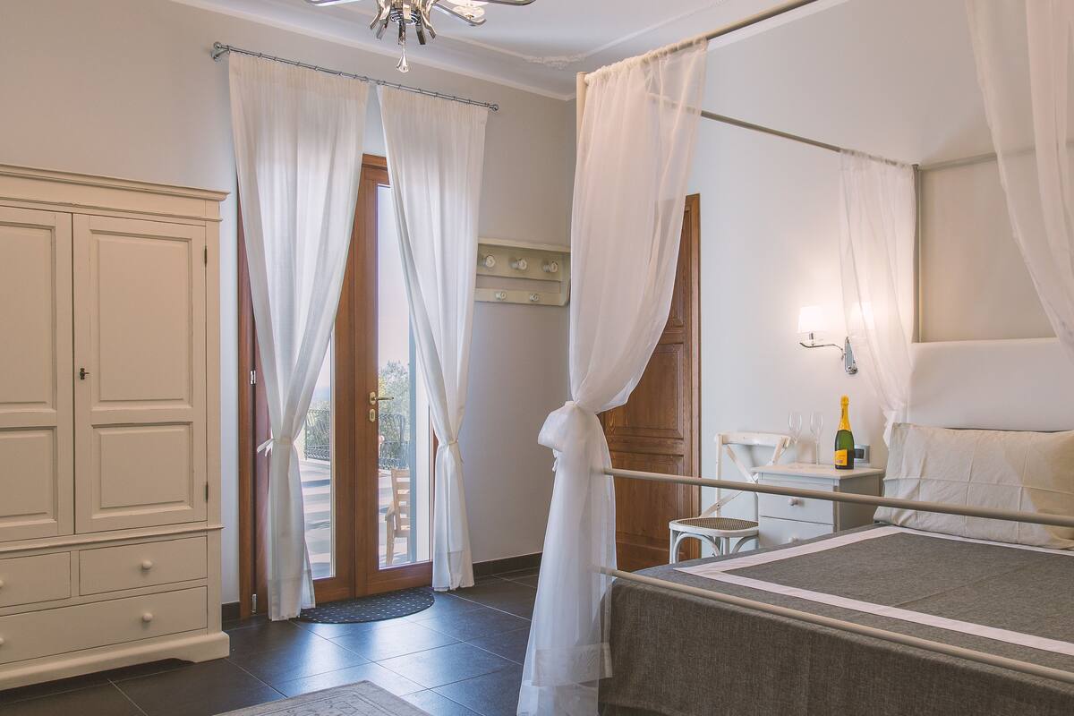 A bedroom with a bed, a wardrobe, a bedside table with a bottle, and a window with curtains.