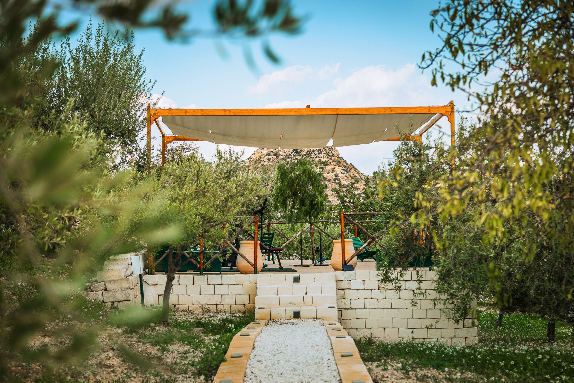 Un espace extérieur aménagé, abrité et doté de sièges, accessible par un sentier en pierre, entouré de verdure et avec une montagne en toile de fond.