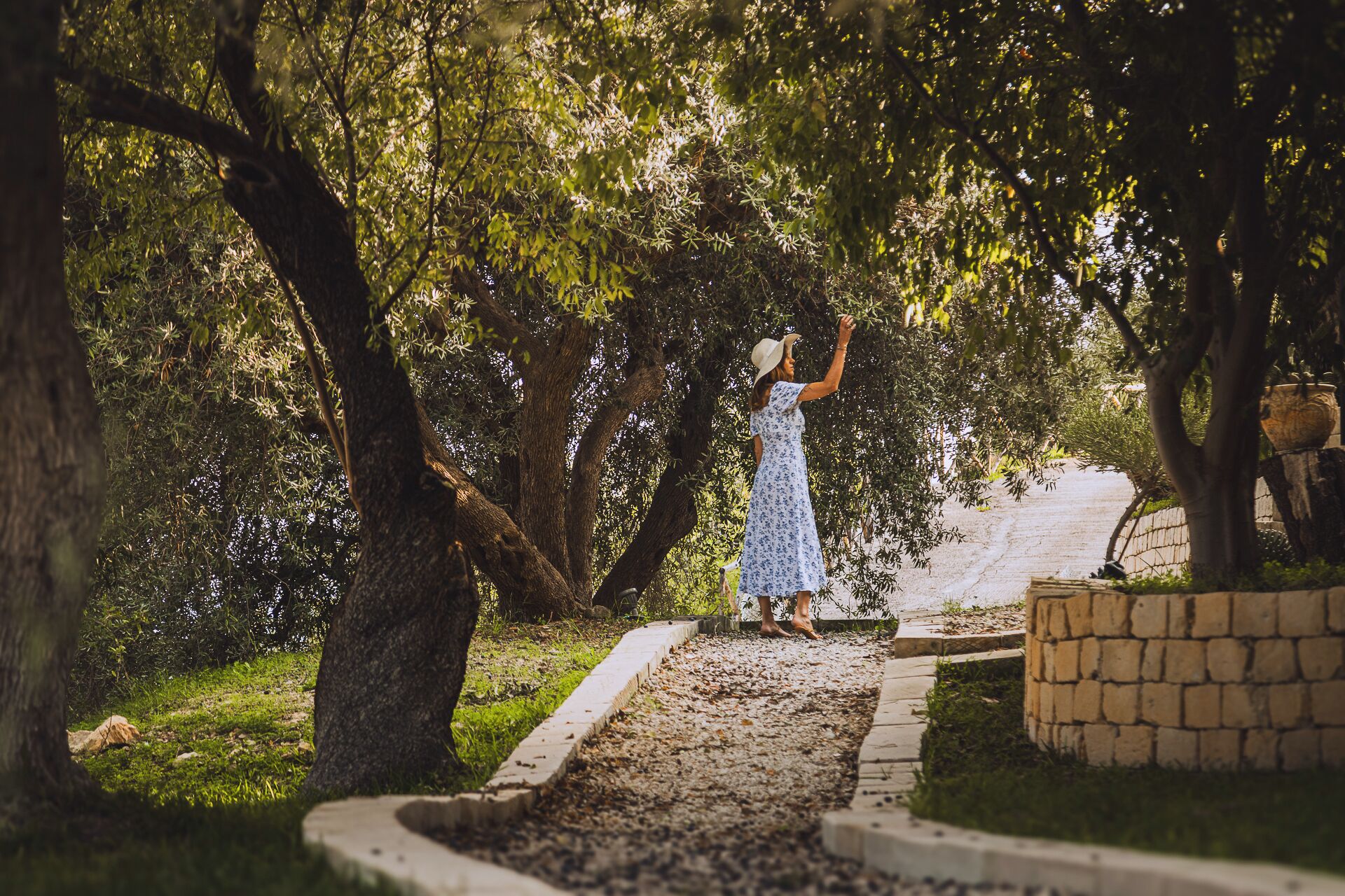 A woman in a white dress standing on a stone pathway surrounded by trees.