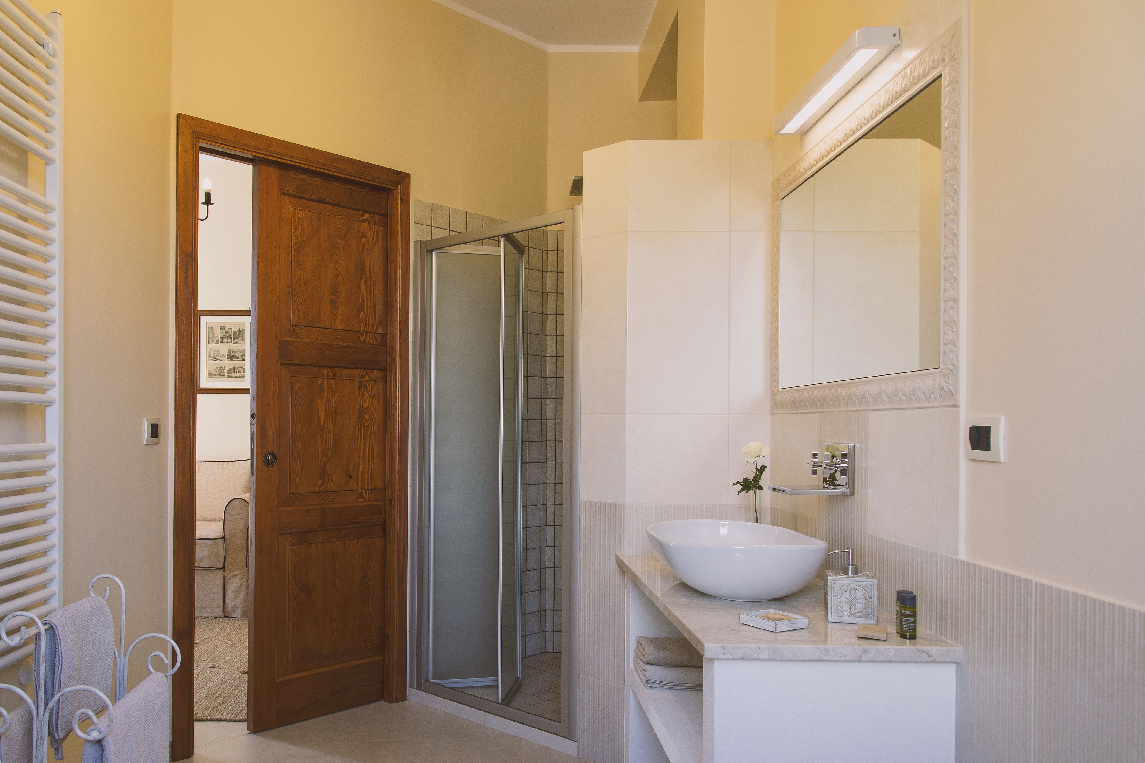 A bathroom with a wooden door, a glass shower enclosure, a white sink, and a mirror.