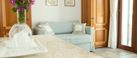 A room with a light blue sofa, a wooden wardrobe, and a vase with purple flowers on a table.