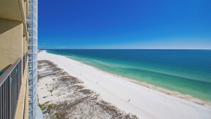 A beach view from a balcony with a clear blue sky, sandy beach, and ocean.