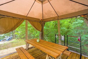 A wooden picnic table under a tent with a view of a forest. - Lakefront 3 Bedroom Cottage - sleeps 6 (Harcourt)