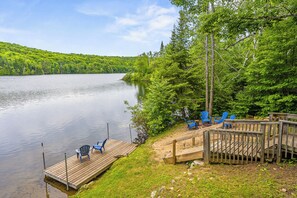 Une jetée en bois avec des chaises bleues, une terrasse en bois et une vue sur un lac entouré d’arbres.