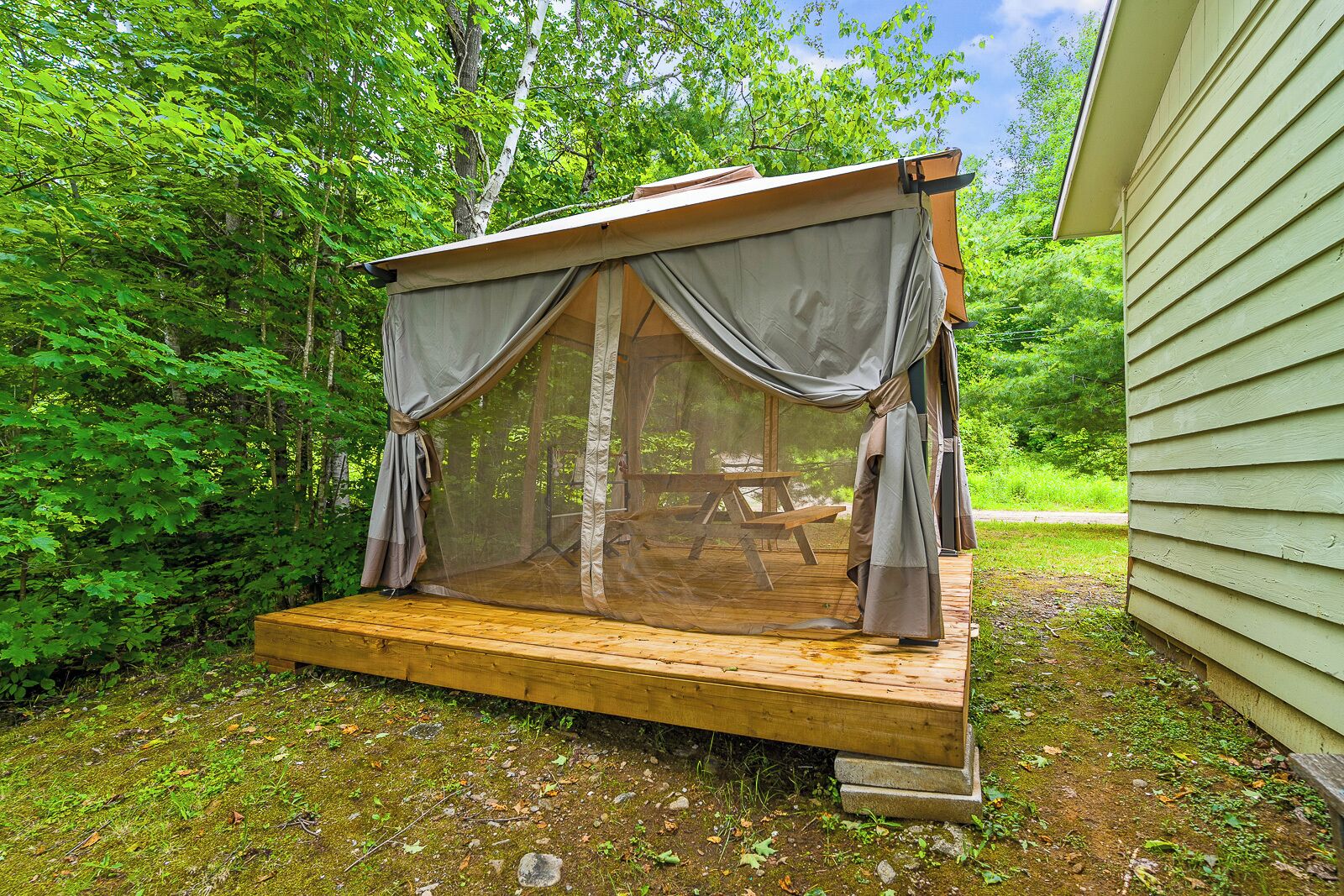 A wooden deck with a covered seating area, surrounded by dense green foliage.