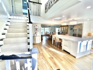 A spacious kitchen with a central island, a dining area with chairs, and a staircase leading to an upper level. - Spectacular Waterfront Cape Cod Home, Oceanfront And Beach,AC,Deck,Grill,Hot Tub (Falmouth)