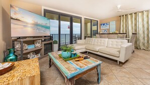 Ein Wohnzimmer mit Fernseher, einer Couch, einem Couchtisch und Blick auf den Strand.