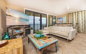 A living room with a television, a sofa, a coffee table, and a view of the beach.