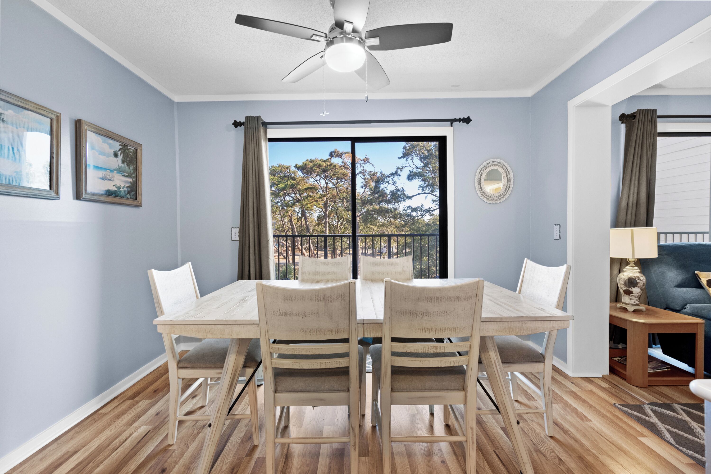 A dining area with a table and chairs, a ceiling fan, and a view through a large window.