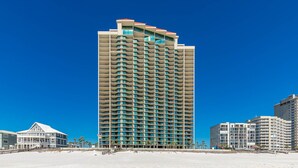 A tall hotel with multiple balconies, located on a beach with other buildings nearby. - Come RELAX on the LAZY RIVER! Phoenix West 3BR (Orange Beach)
