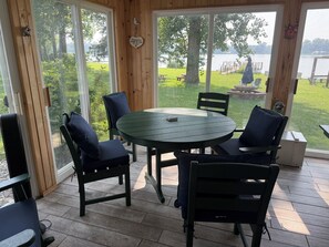 Une terrasse couverte avec une table ronde et quatre chaises, de grandes fenêtres et une vue sur un lac et une zone verdoyante.