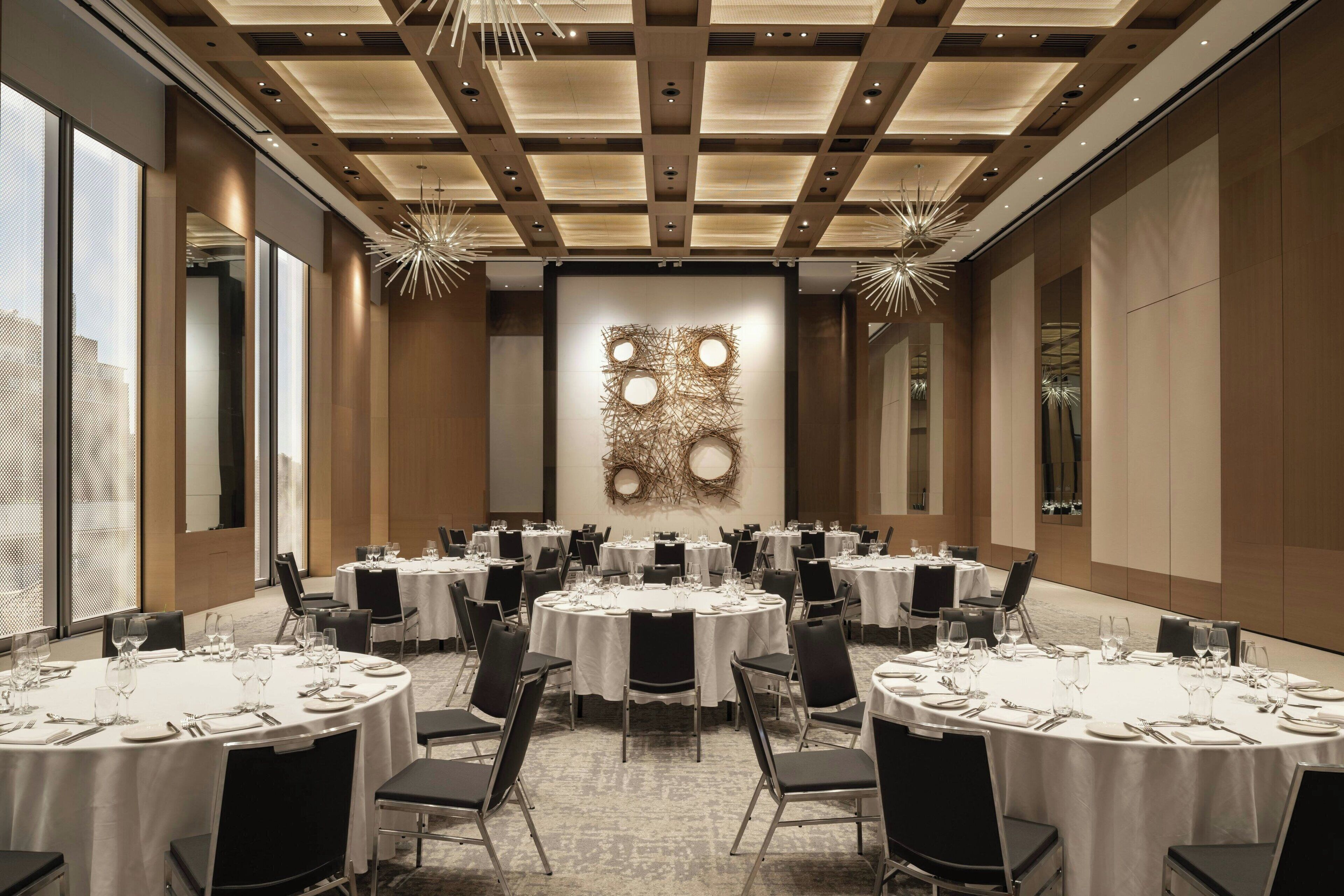 A conference room with round tables, black chairs, and a large abstract wall art piece.