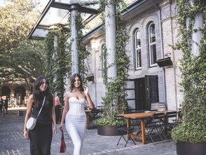 An outdoor cafe area with a brick building, outdoor seating, and greenery.