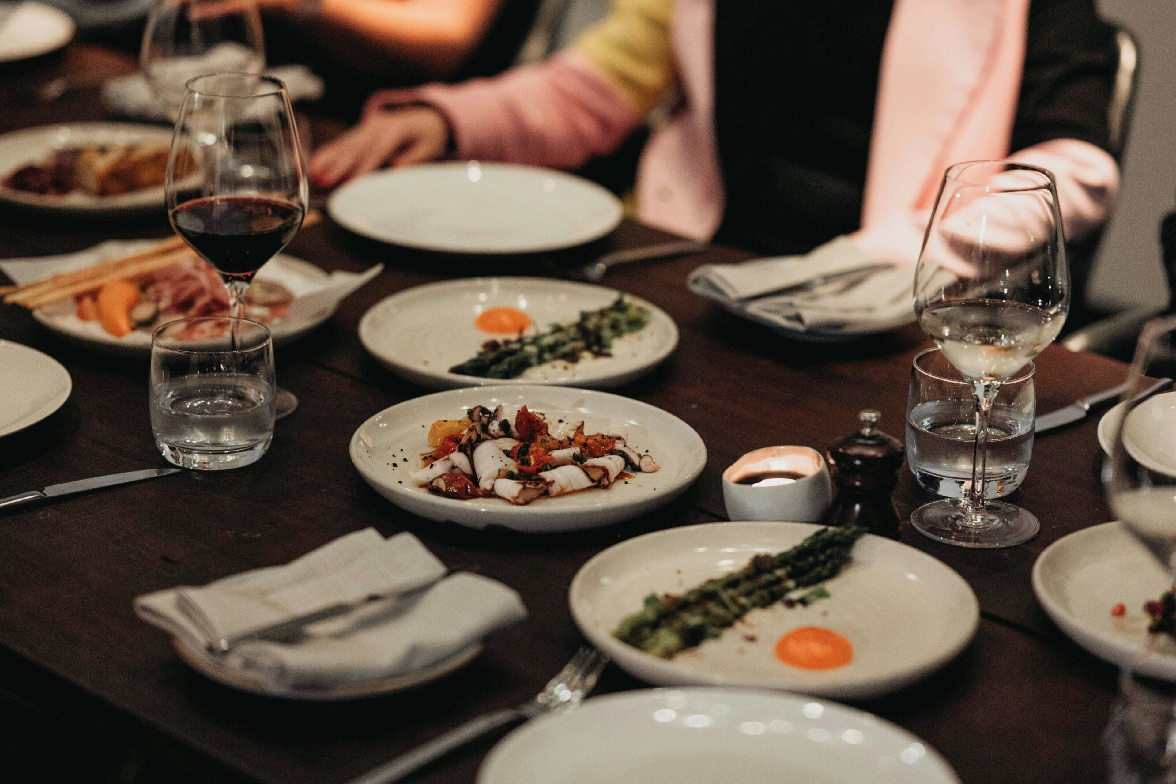 Une table à manger dressée avec des assiettes remplies de nourriture, des verres d’eau et une bougie.