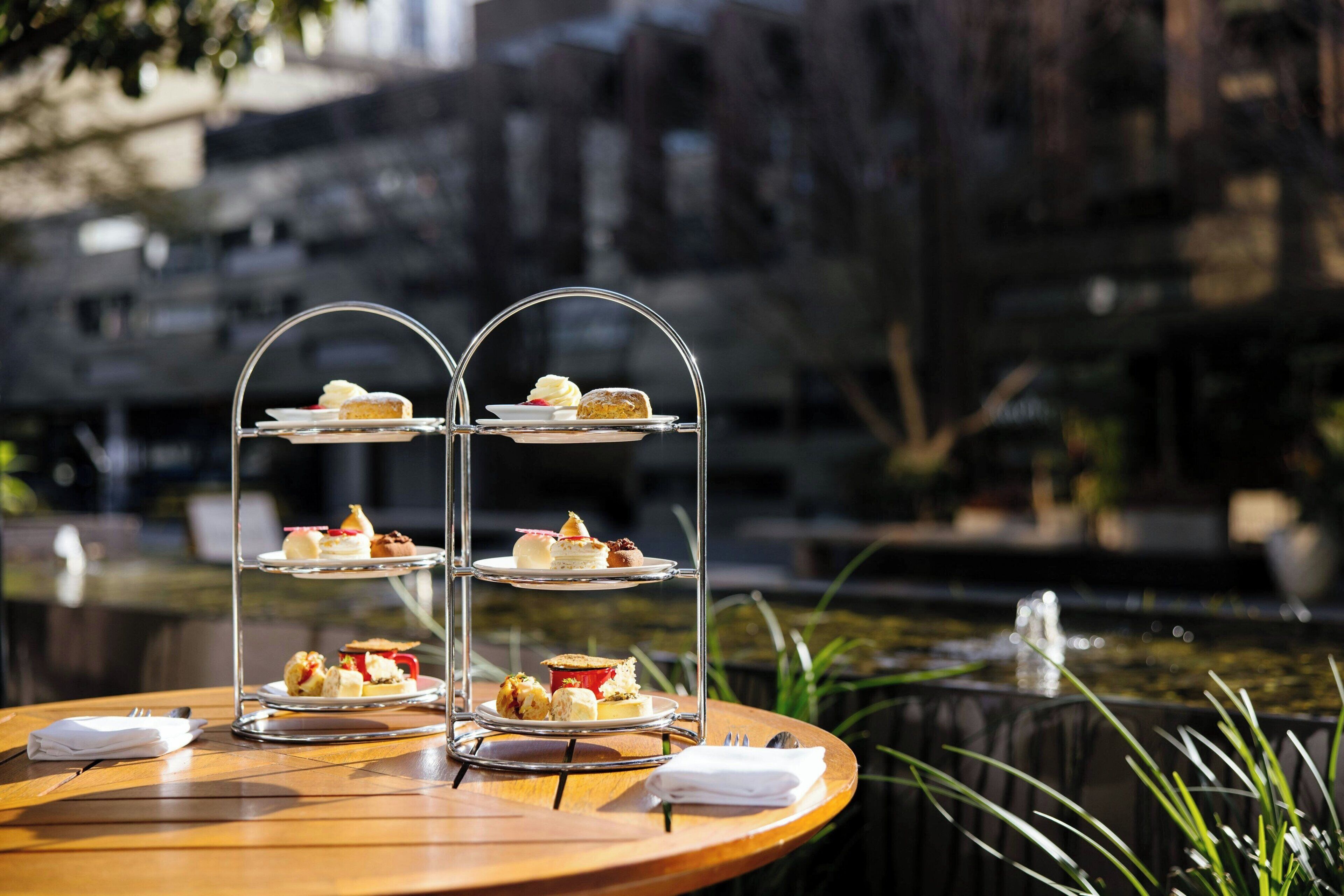 Un soporte de tres niveles para postres con diferentes pasteles sobre una mesa de madera cerca de una fuente.