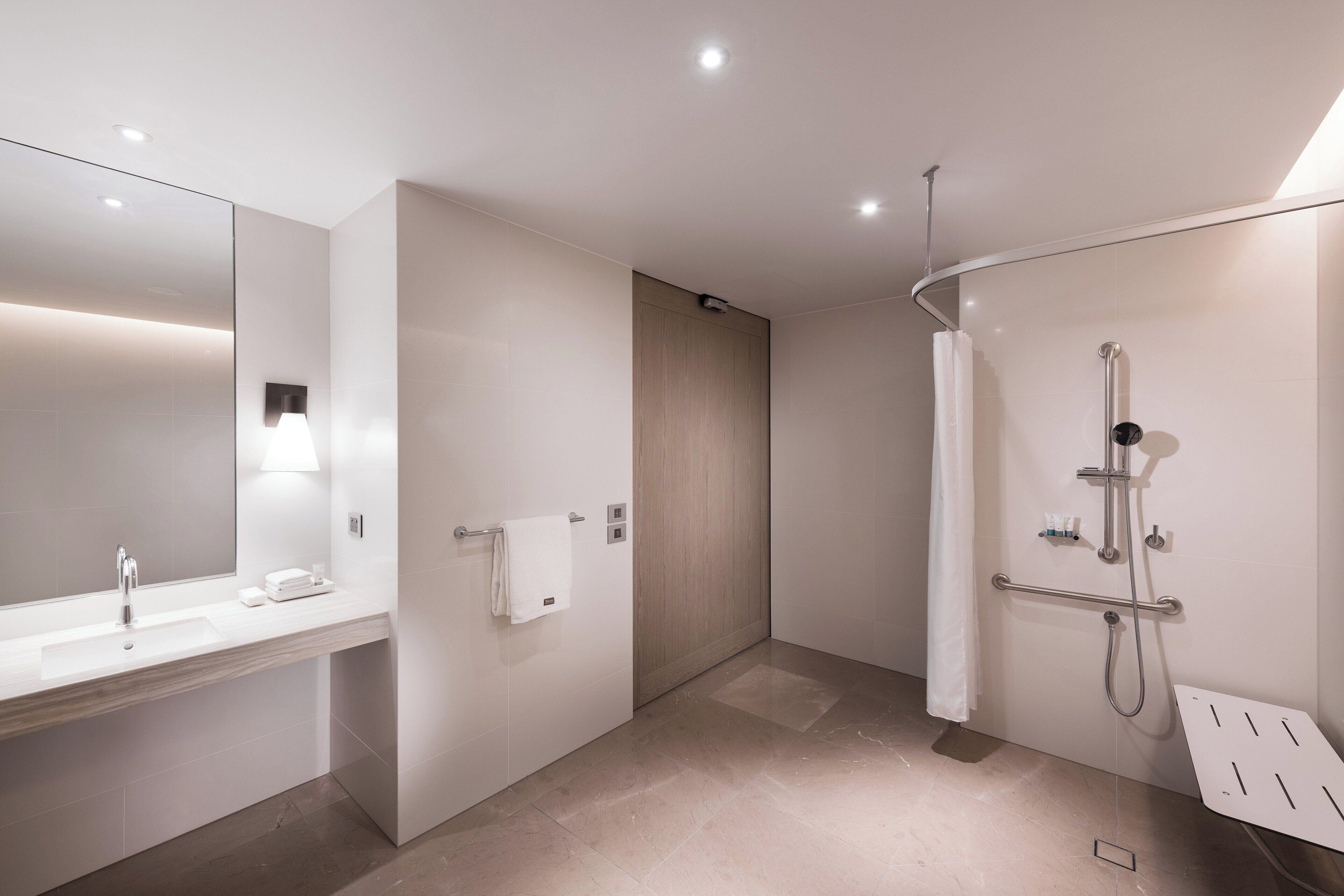 A modern bathroom with a large mirror, a sink, a shower, and a towel rack.