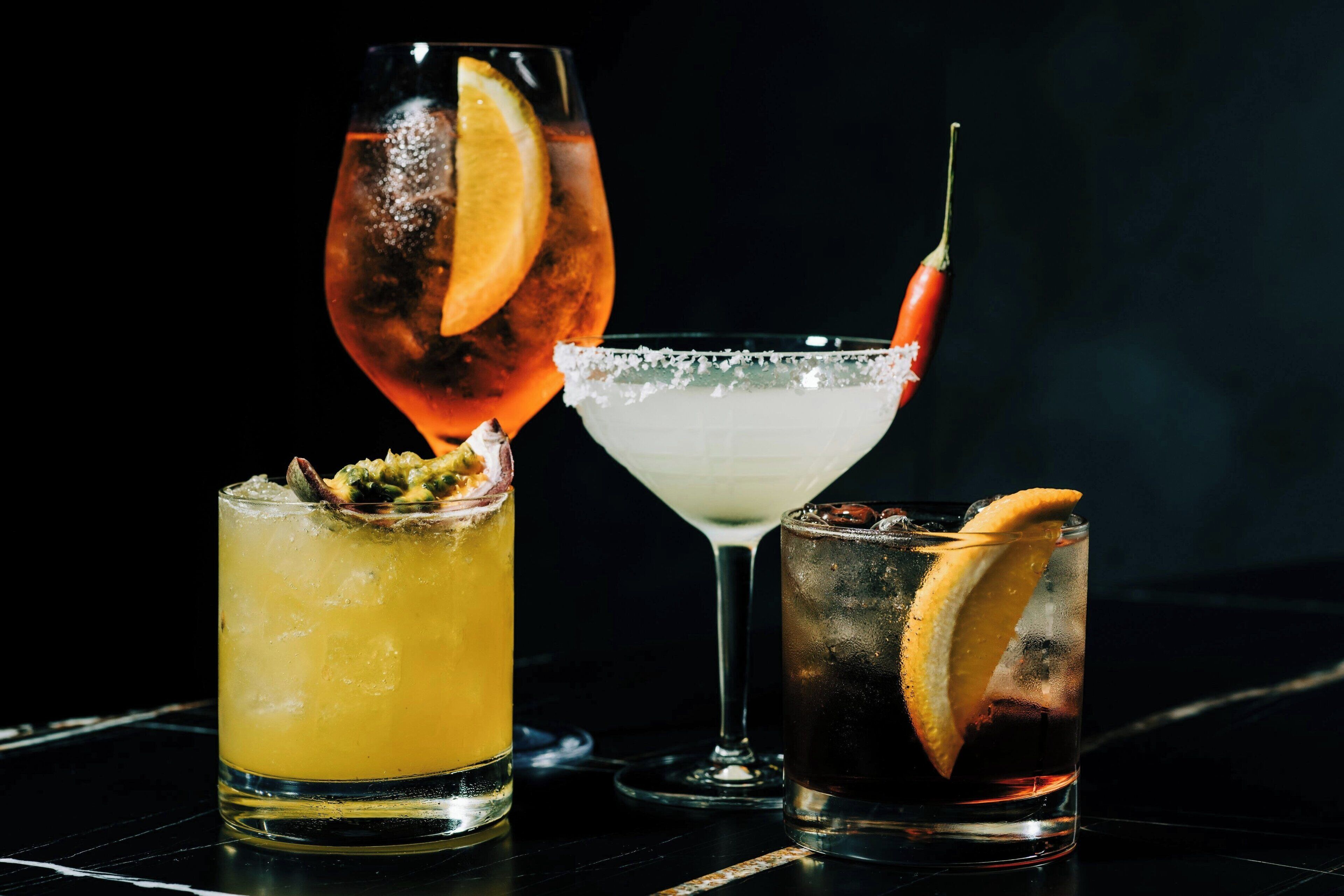 Three different cocktails in glasses with ice and garnishes.