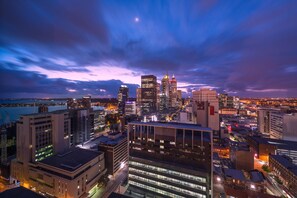 A cityscape at dusk with illuminated buildings and a body of water in the foreground. - The Westin Perth (Perth)