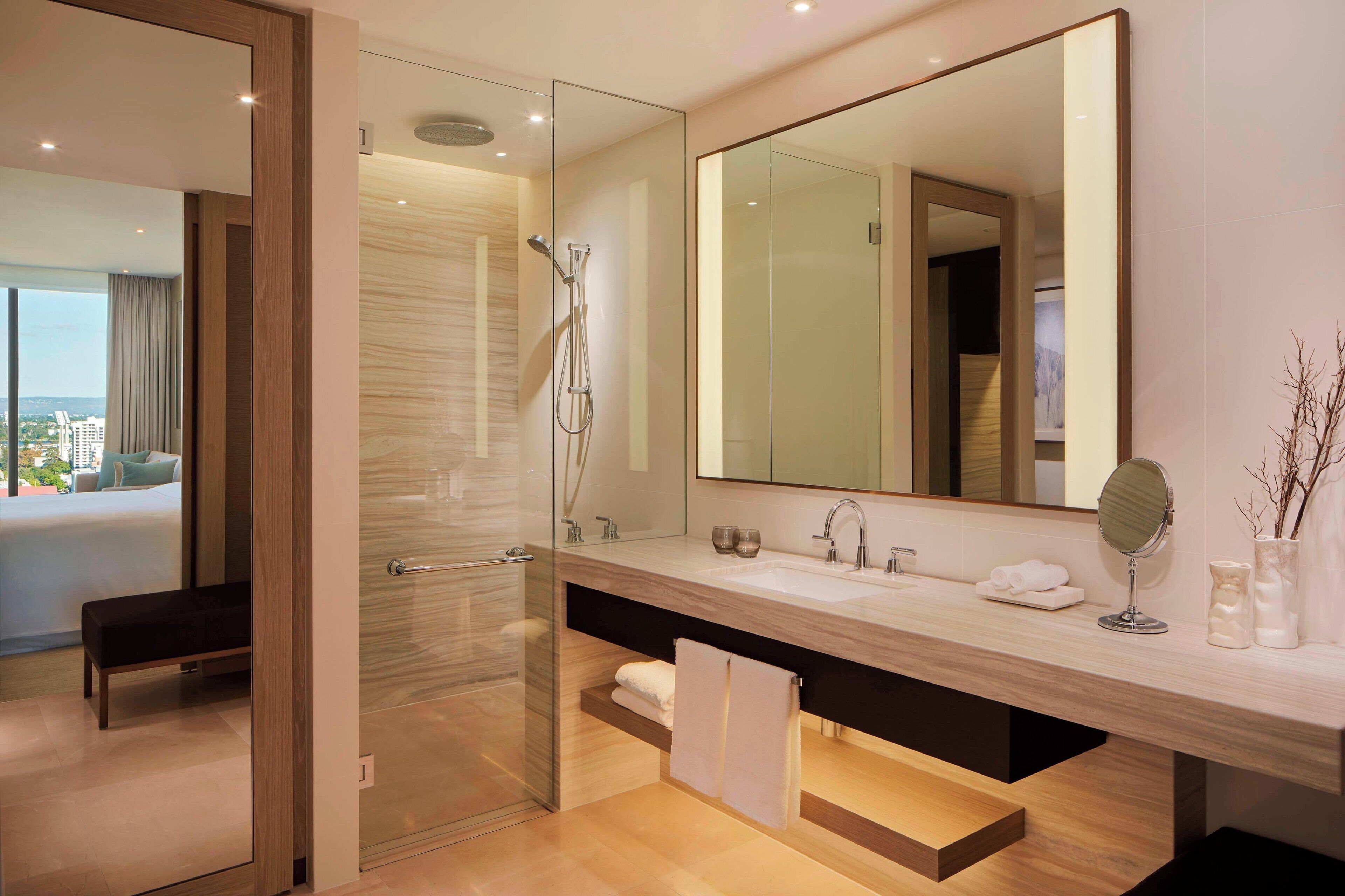 Un baño moderno con ducha de vidrio, un espejo grande y un tocador de madera.