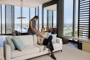A modern living room with a sofa, a dining table, and large windows offering a city view. - The Westin Perth (Perth)