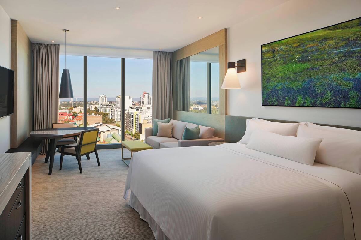 Quarto de hotel com uma cama grande, uma escrivaninha, uma cadeira e vista para a cidade.