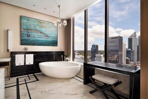 A modern bathroom with a large bathtub, a city view, and a large painting on the wall.