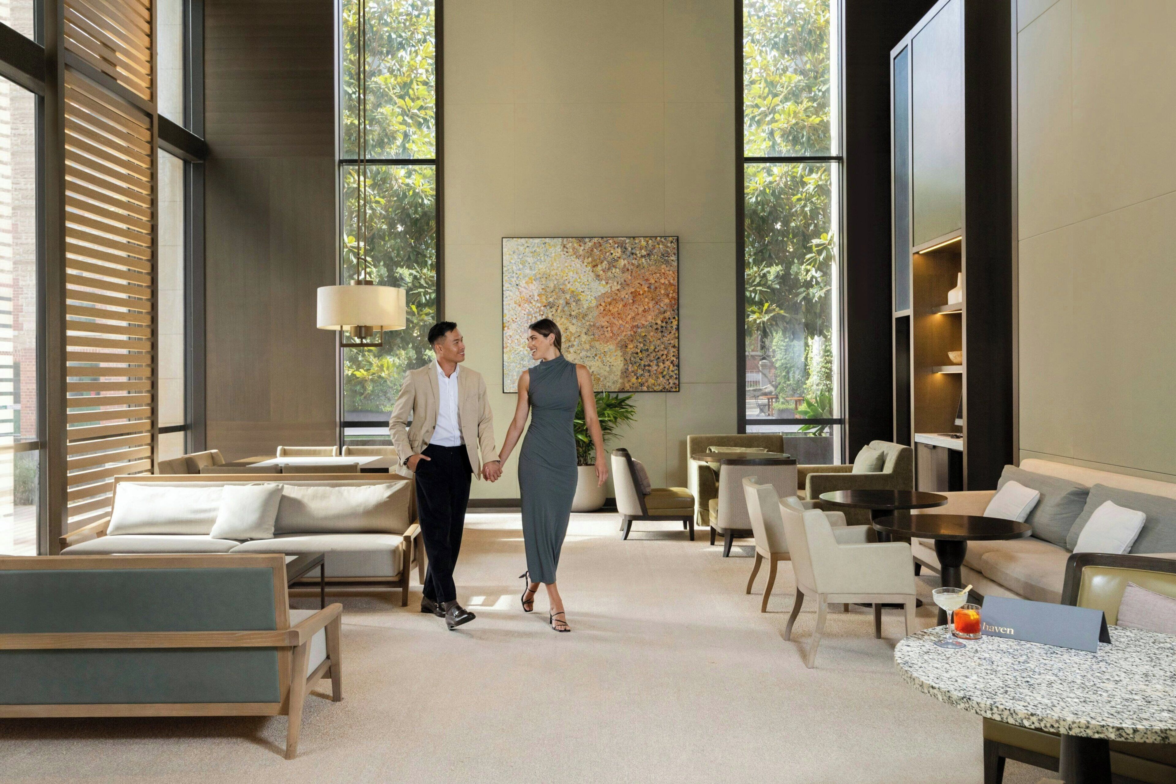 Un hall d’hôtel moderne, doté d’espaces aménagés avec des sièges, d’une grande fenêtre et d’un tableau accroché au mur.
