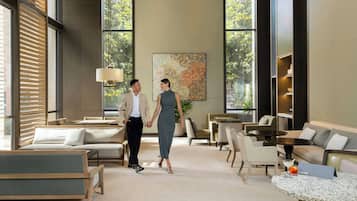 A modern hotel lobby with seating areas, a large window, and a painting on the wall.