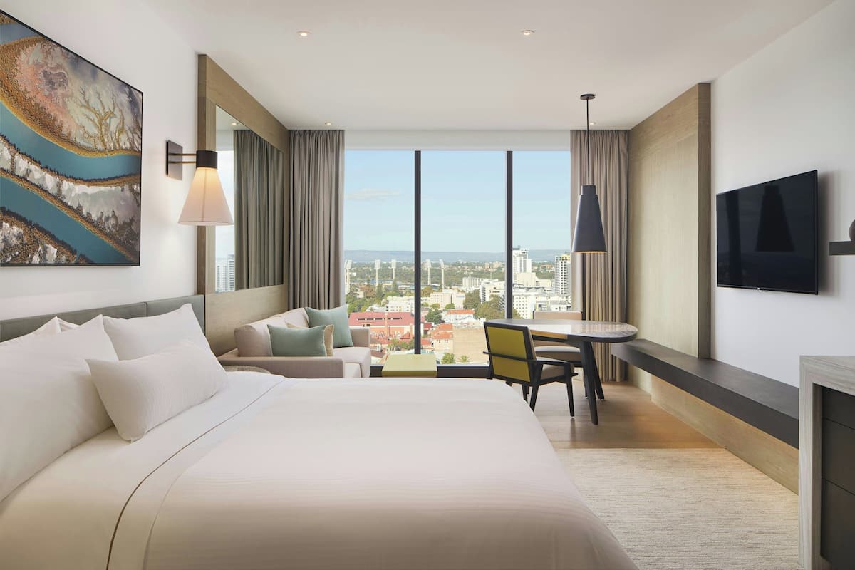 Quarto de hotel moderno com uma cama grande, um sofá, uma mesa de jantar e uma televisão.