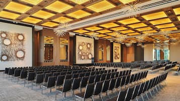 Uma sala de conferência com fileiras de cadeiras, teto de madeira com iluminação embutida e obras de arte abstratas nas paredes.