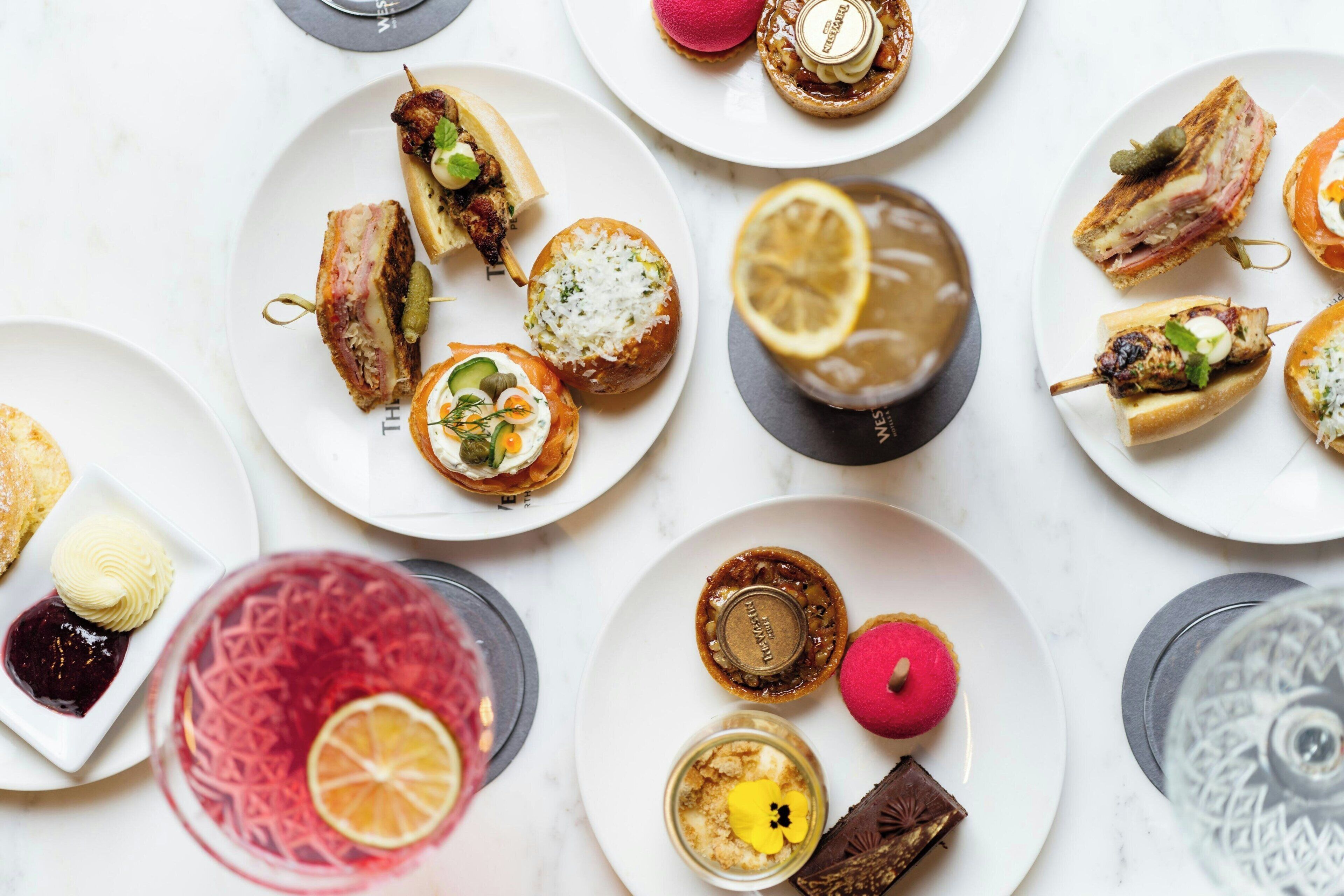 A variety of food items on plates, including sandwiches, skewers, and desserts.