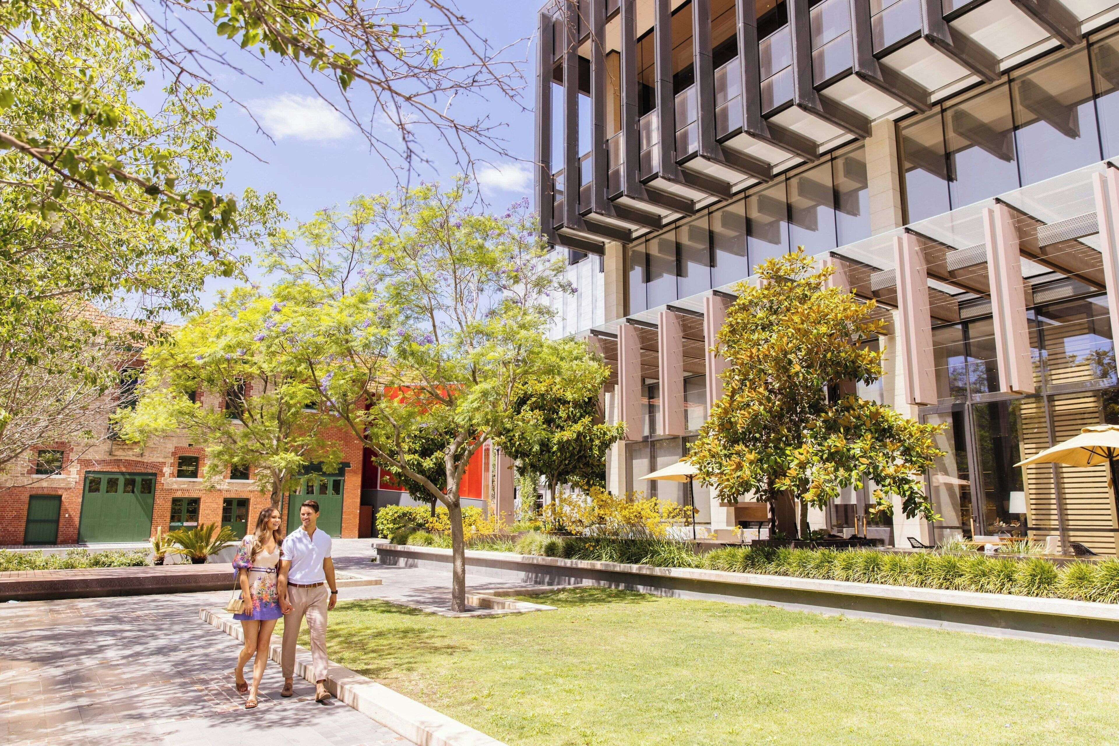 A modern building with a glass facade and a courtyard with trees and seating areas.