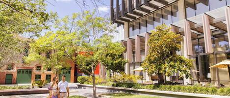 A modern building with a glass facade and a courtyard with trees and seating areas.