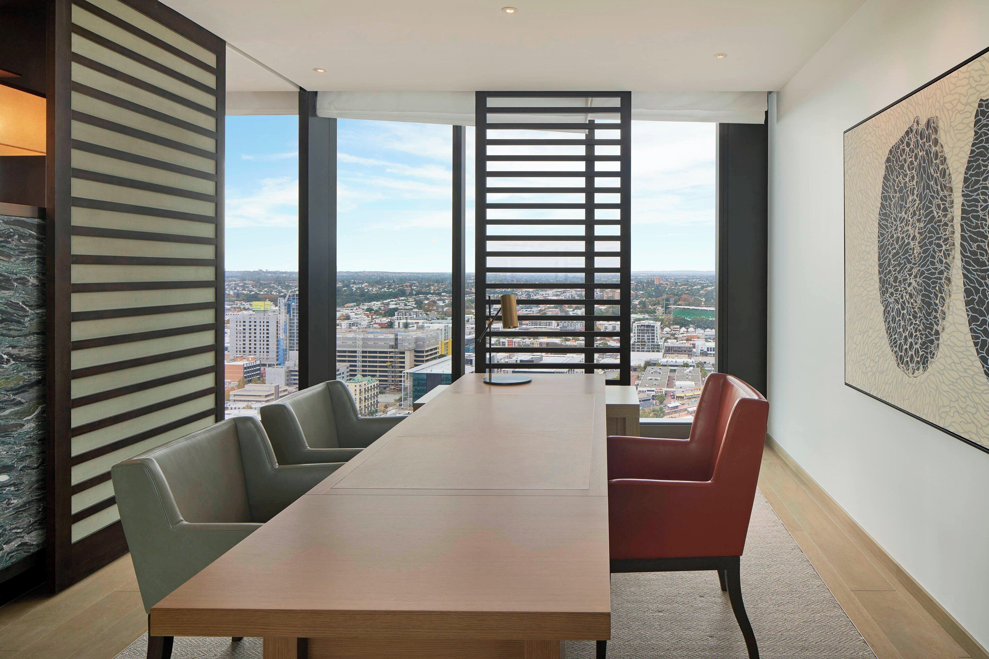 A conference room with a long table, chairs, and a view of a cityscape through large windows.