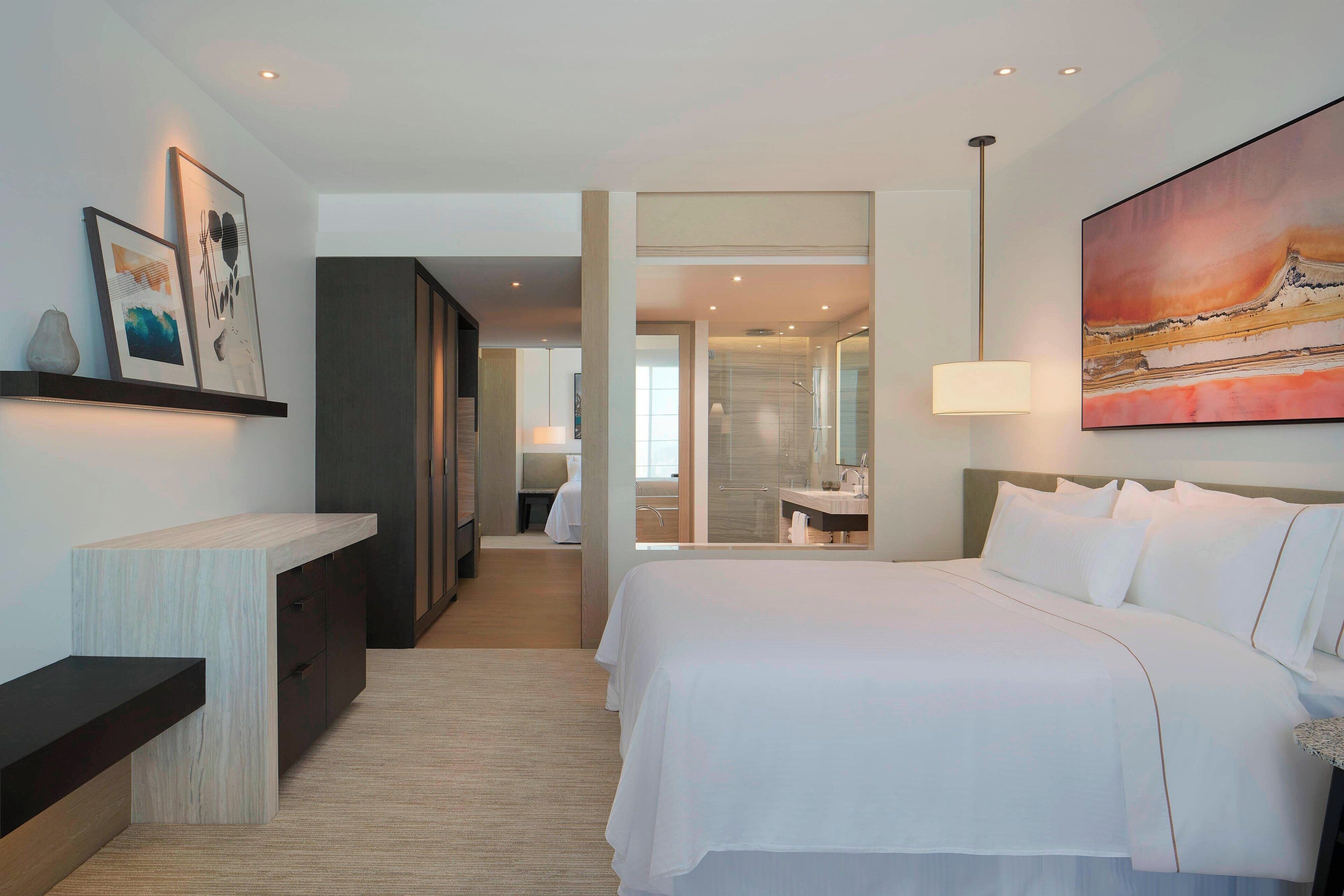 A modern hotel room with a large bed, a desk, and a bathroom visible through an open door.