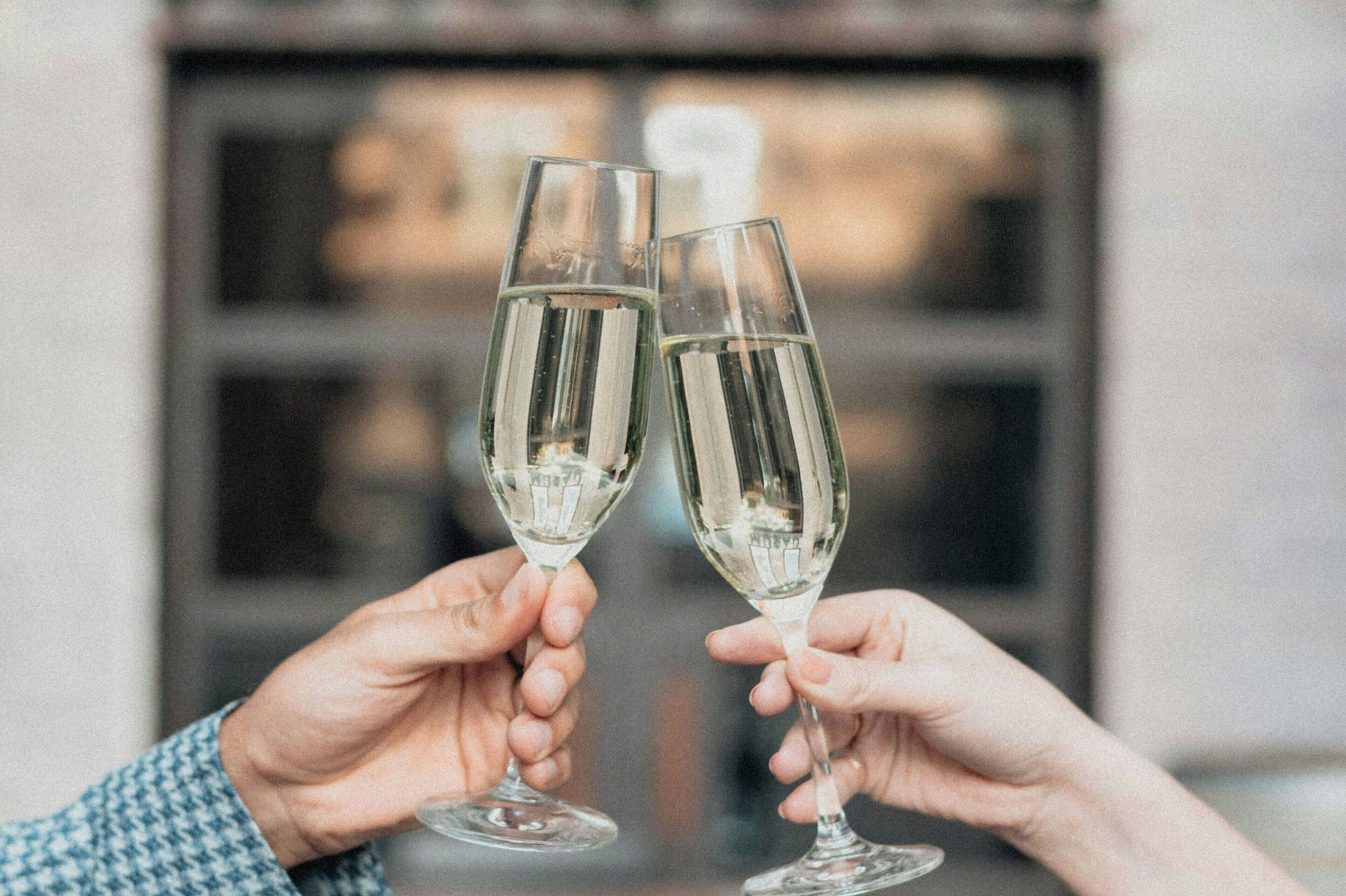 Two hands holding champagne flutes in a toast.