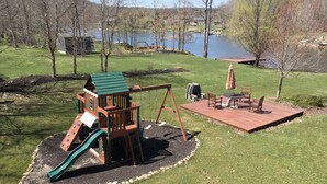 Un parque infantil con tobogán, columpios y una mesa de picnic con sillas y una sombrilla.