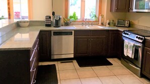 Una cocina con lavavajillas, estufa, microondas y ventana con vistas al paisaje verde exterior.