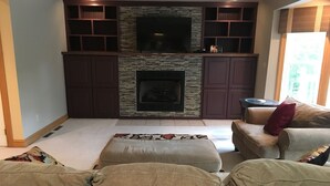 Una sala de estar con chimenea de piedra, armarios de madera oscura y un televisor de pantalla plana grande.