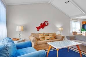 Uma sala de estar com sofá bege, poltronas azuis, mesa de centro e um detalhe decorativo vermelho na parede.