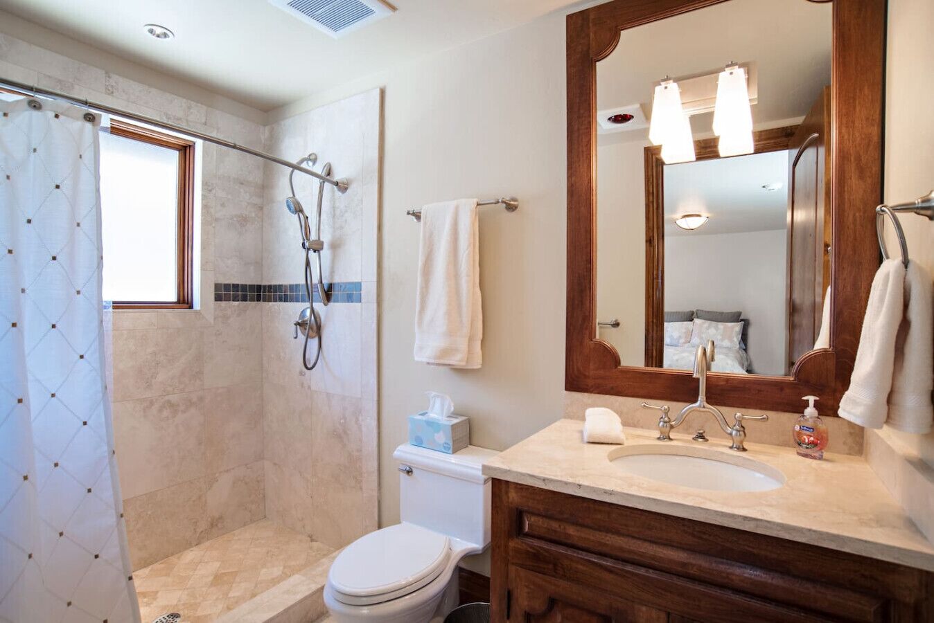 Et badeværelse med brusebad, toilet, vask og et stort spejl.