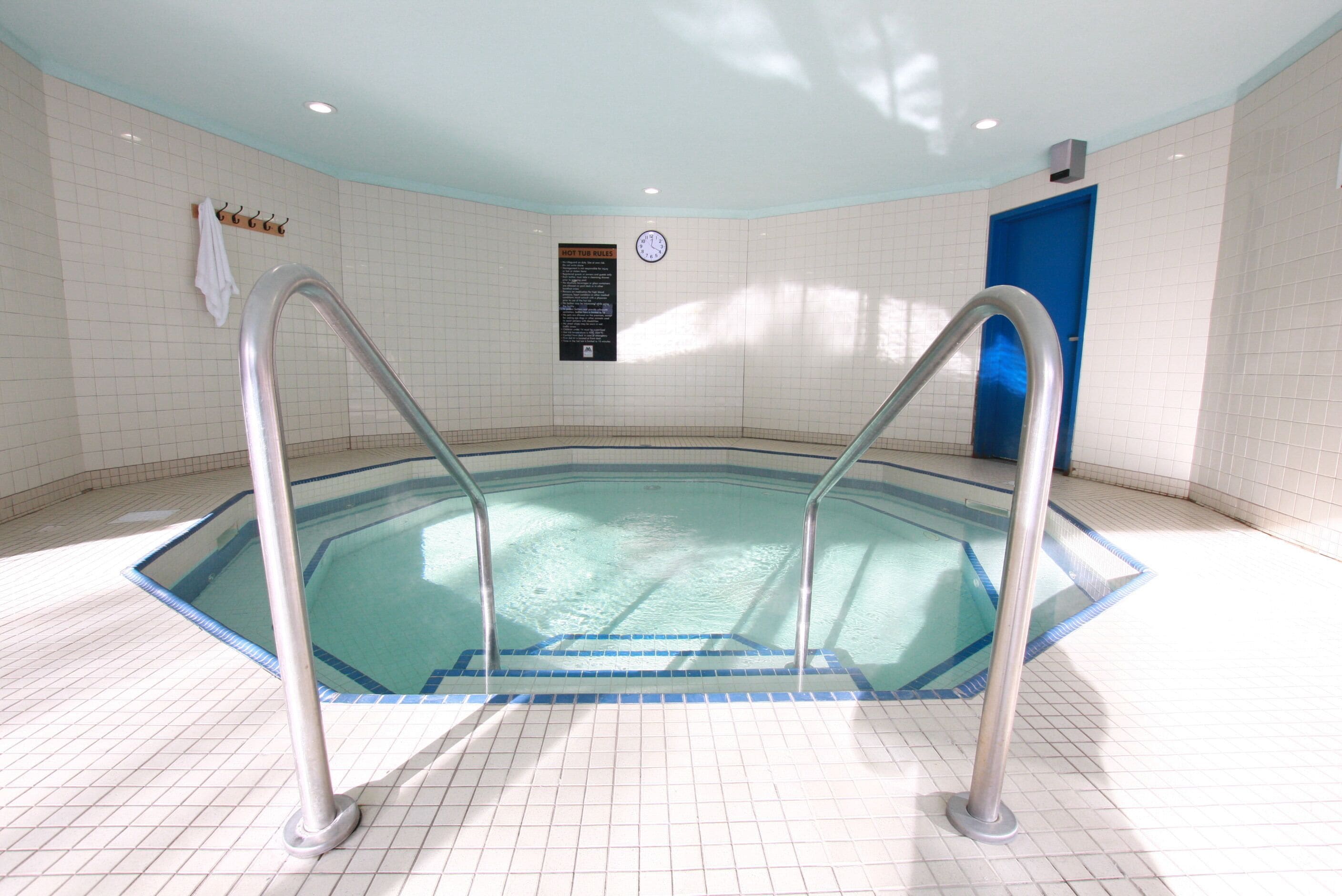 En swimmingpool med metallstegar, en klocka och en blå dörr.