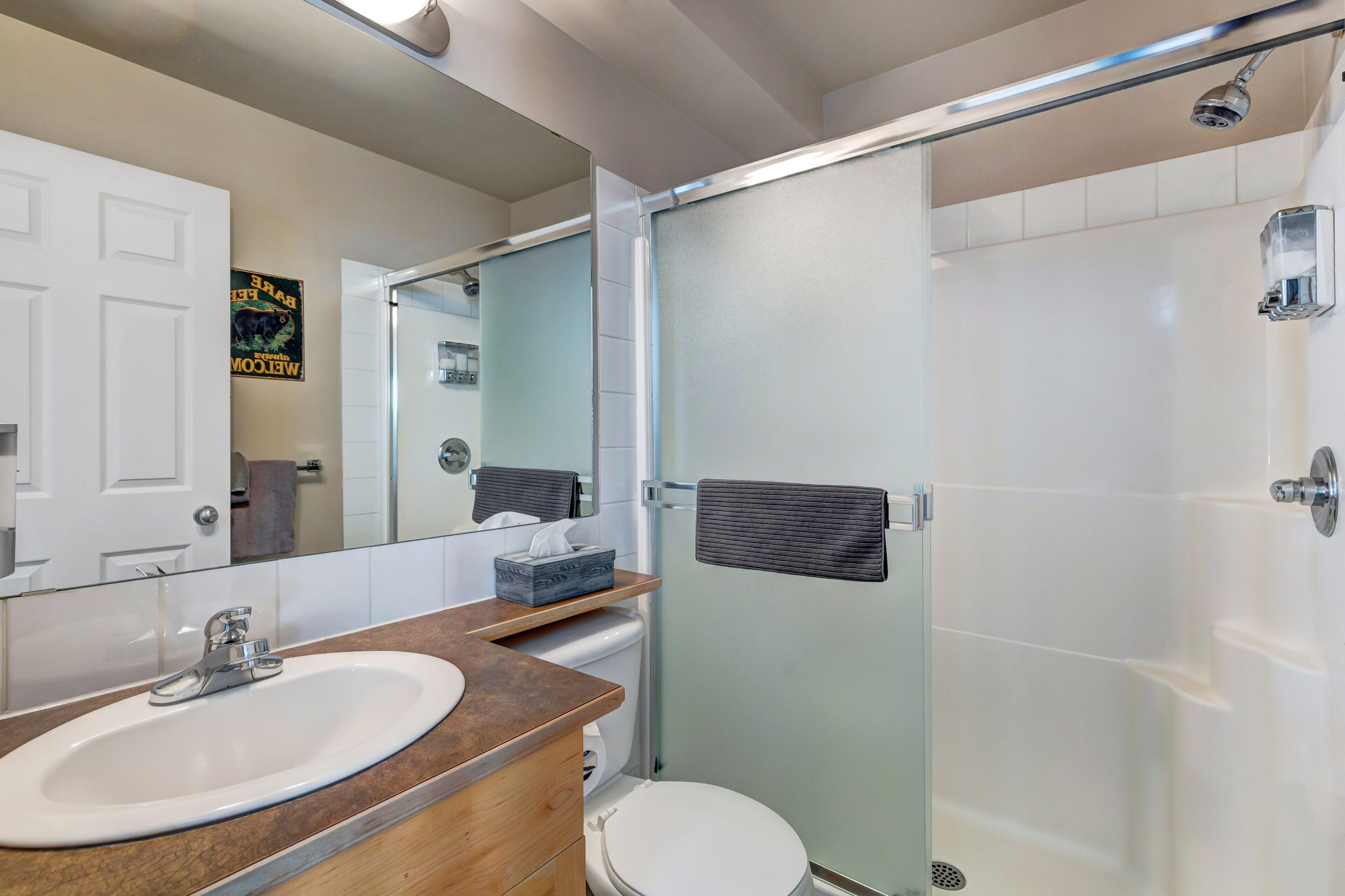 Une salle de bain moderne avec un lavabo blanc, un miroir, une cabine de douche en verre et des toilettes.