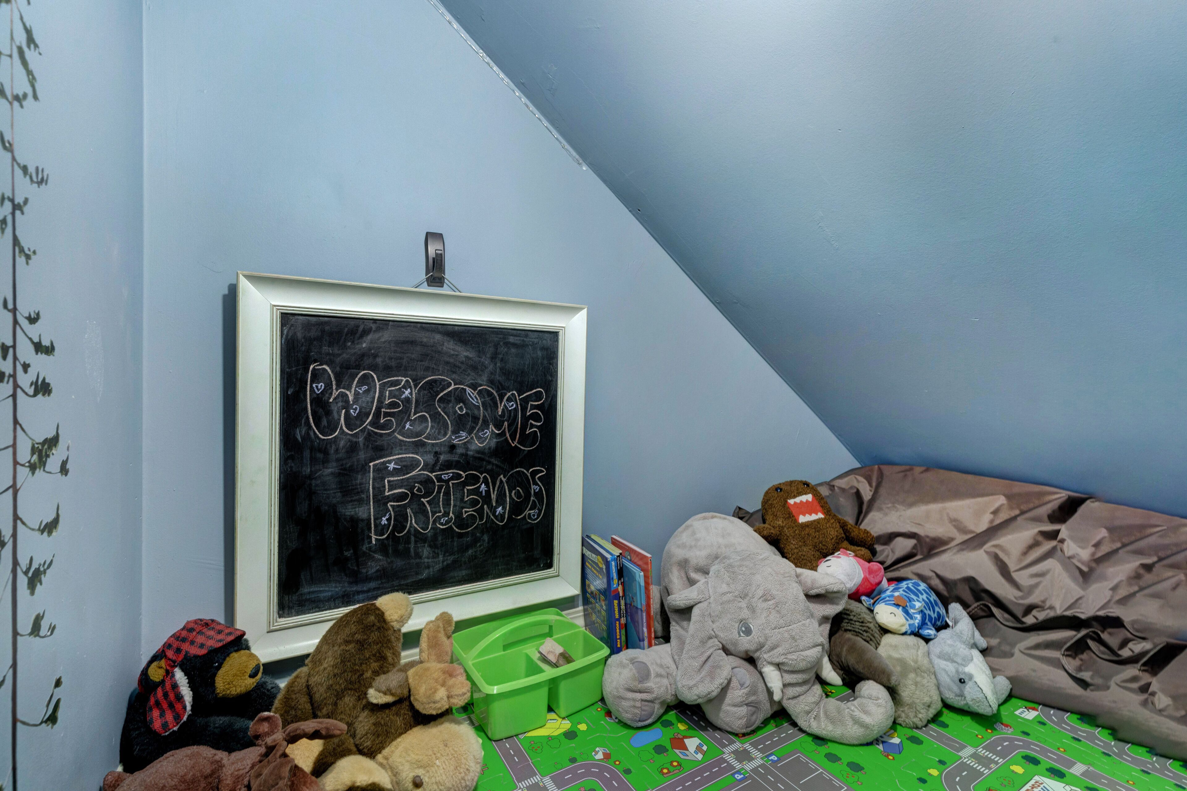 A room with a chalkboard displaying "WELCOME FRIENDS," stuffed animals, and a green play mat.